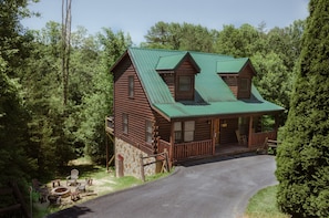 Situated in a lush forest, this cabin features a rustic design and a spacious porch with outdoor seating.