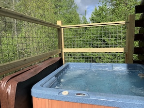 Relax in a serene outdoor setting with a hot tub surrounded by lush greenery.