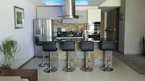 A modern kitchen with a central island, bar stools, and a stainless steel range hood.