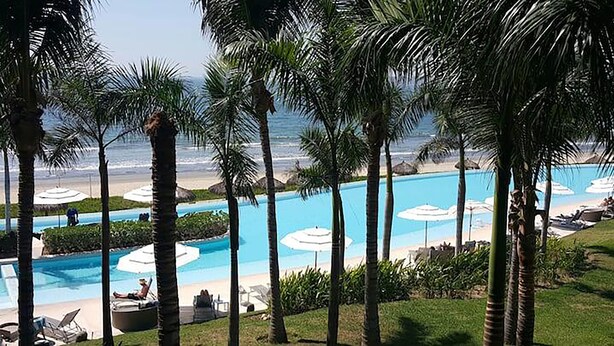 A resort pool with palm trees, lounge chairs, and umbrellas.