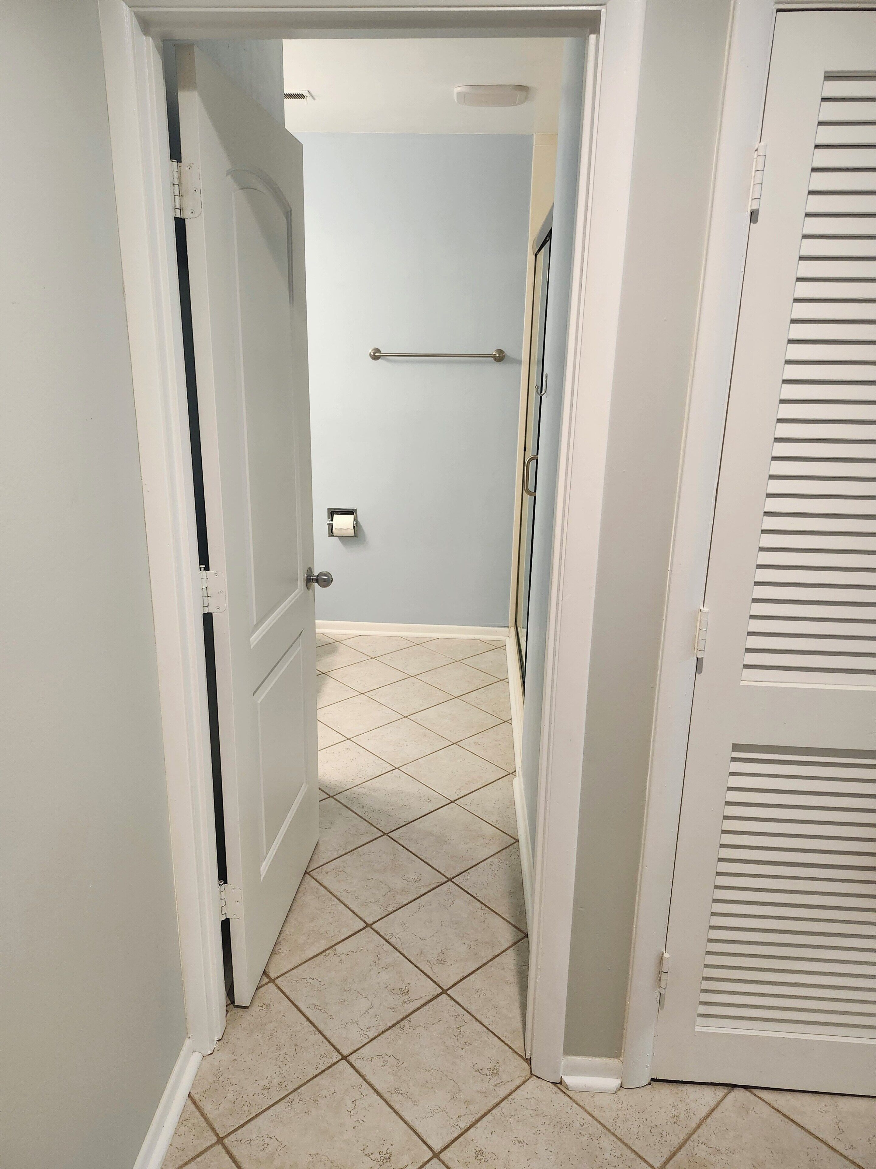 A hallway with a tiled floor, a door with a towel rack, and a toilet paper dispenser.