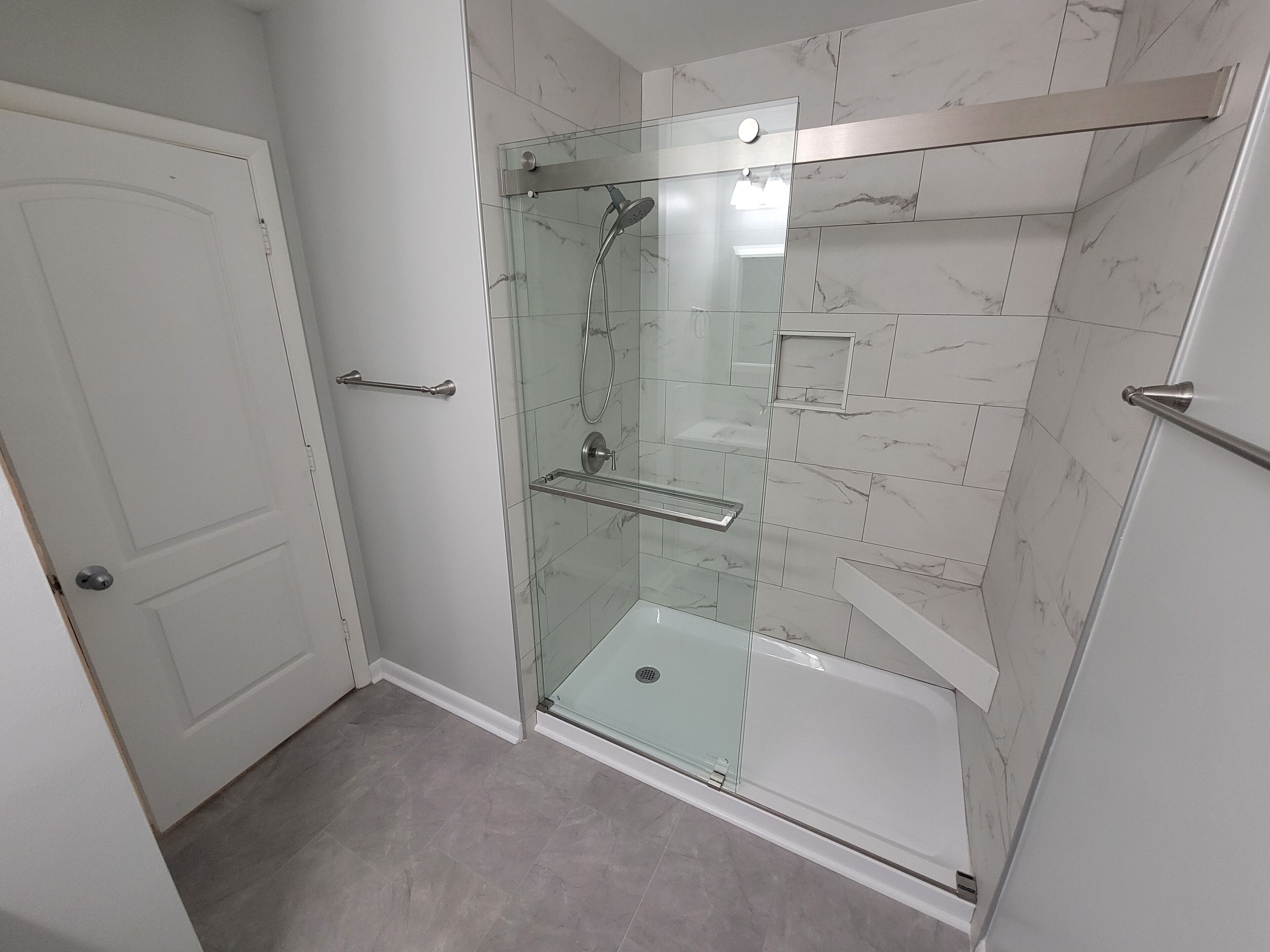 Un baño moderno con ducha de vidrio, azulejos de mármol y puerta blanca.