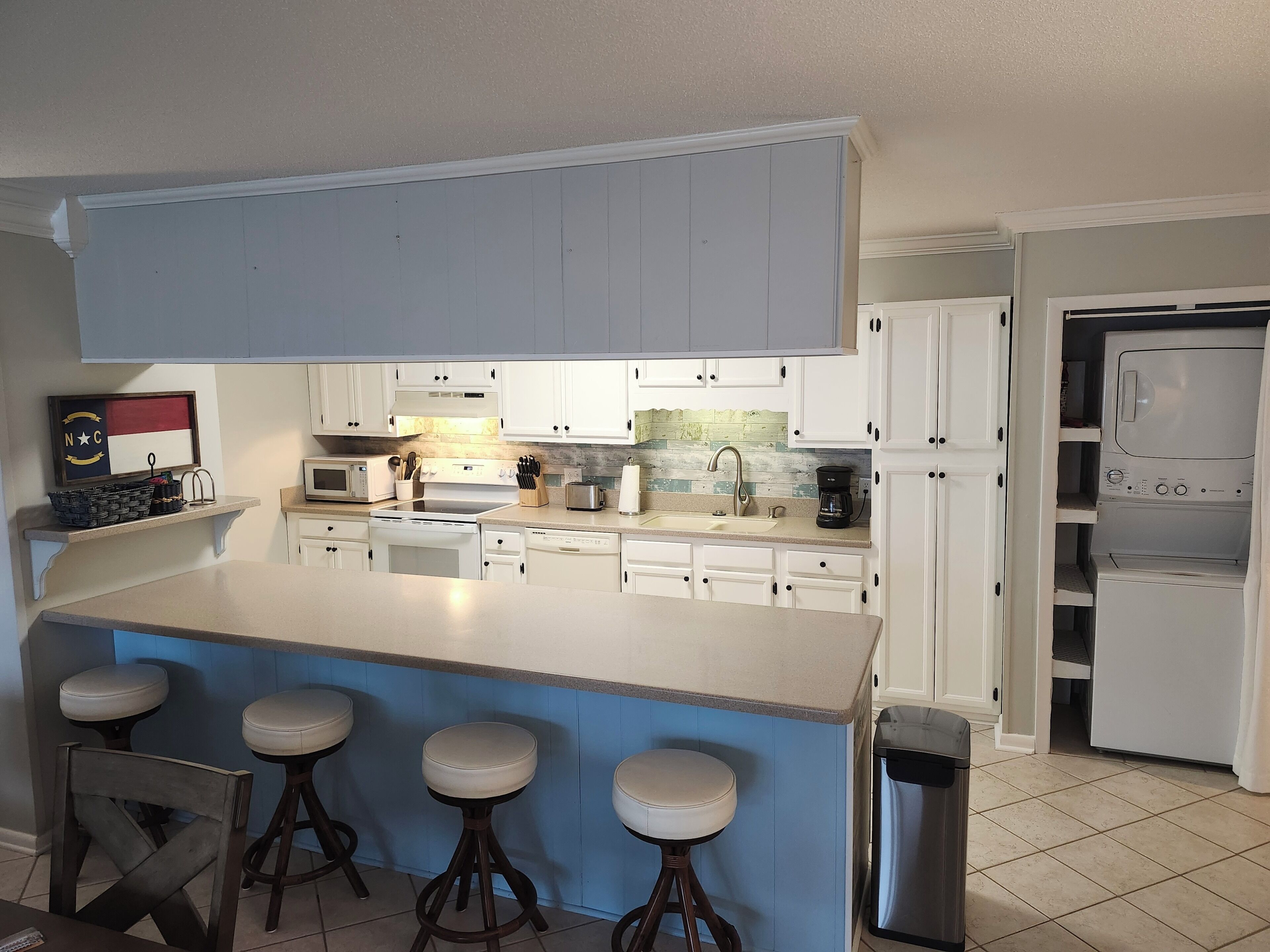 A kitchen with white cabinets, a large island with stools, a microwave, a coffee maker, and a refrigerator.