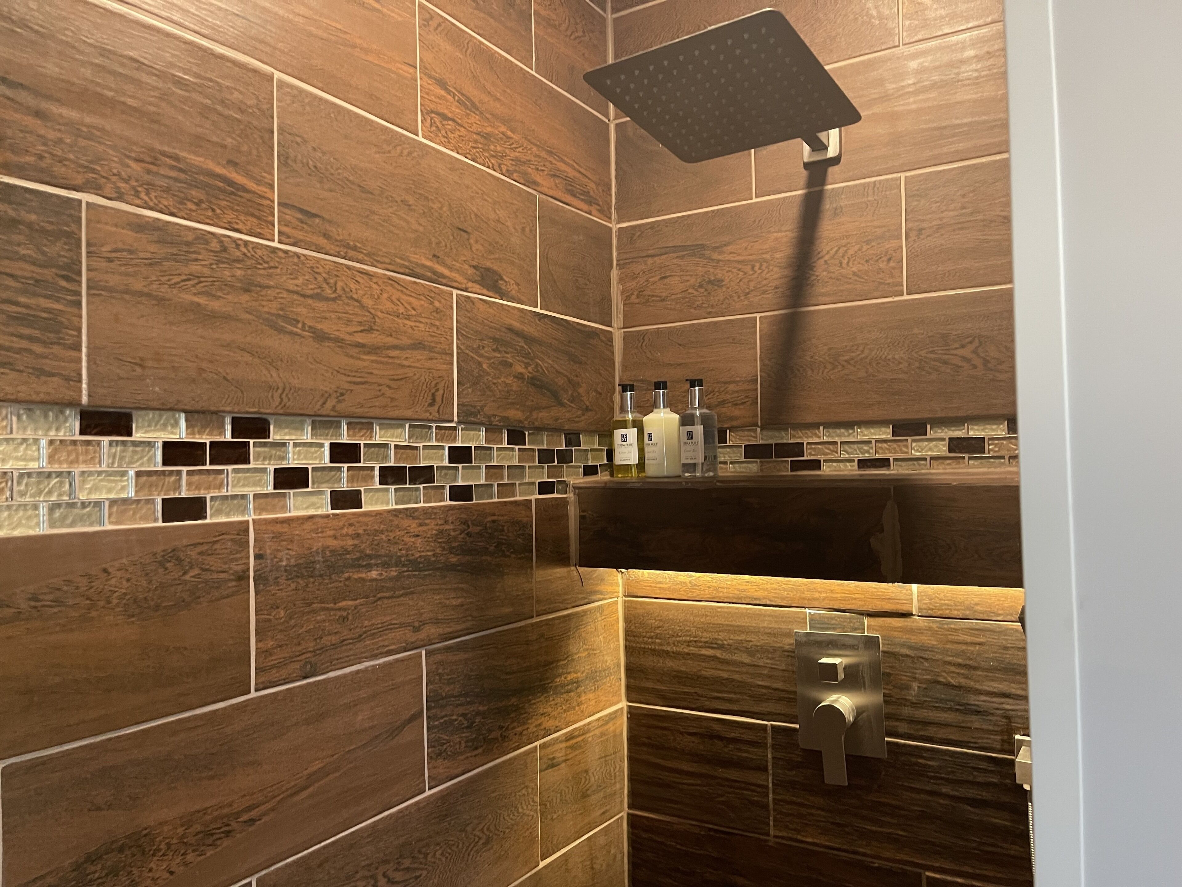 Ein Badezimmer mit Holzbodenfliesen, einer Duschbrause und einem Seifenspender an der Wand.