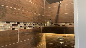 Ein Badezimmer mit Holzbodenfliesen, einer Duschbrause und einem Seifenspender an der Wand.