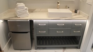 Een compacte keuken met een ingebouwd spoelbakje, een roestvrijstalen koelkast en een marmeren aanrechtblad.