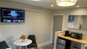 A modern kitchen with a dining area, including a TV displaying content, a small refrigerator, a microwave, and a trash bin. - Suite 201 "The Golden Eagle" (Custer)