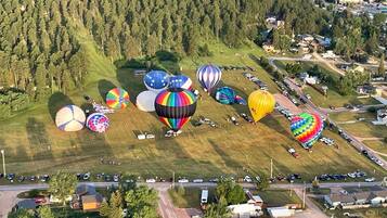 Vista aérea de una zona residencial con varios globos aerostáticos multicolores estacionados en un campo cubierto de césped.