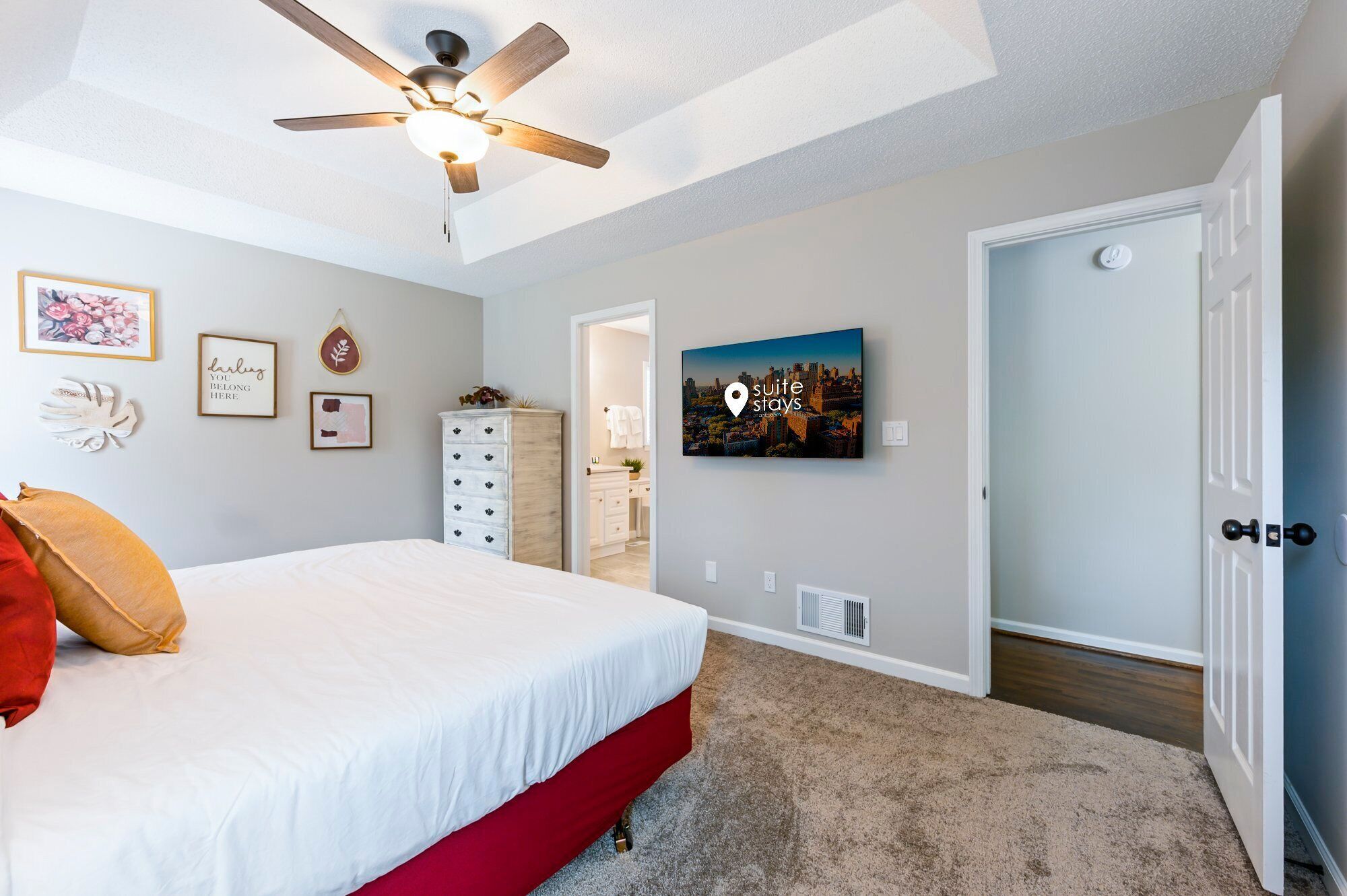 Een slaapkamer met een bed, een plafondventilator, een dressoir, een deur en een aan de muur bevestigd schilderij.