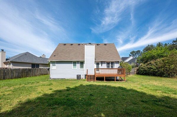 A single-story house with a front deck, a fenced yard, and a clear sky. - Animal Friendly 3BR Stylish Escape, Near LakePoint (Cartersville)