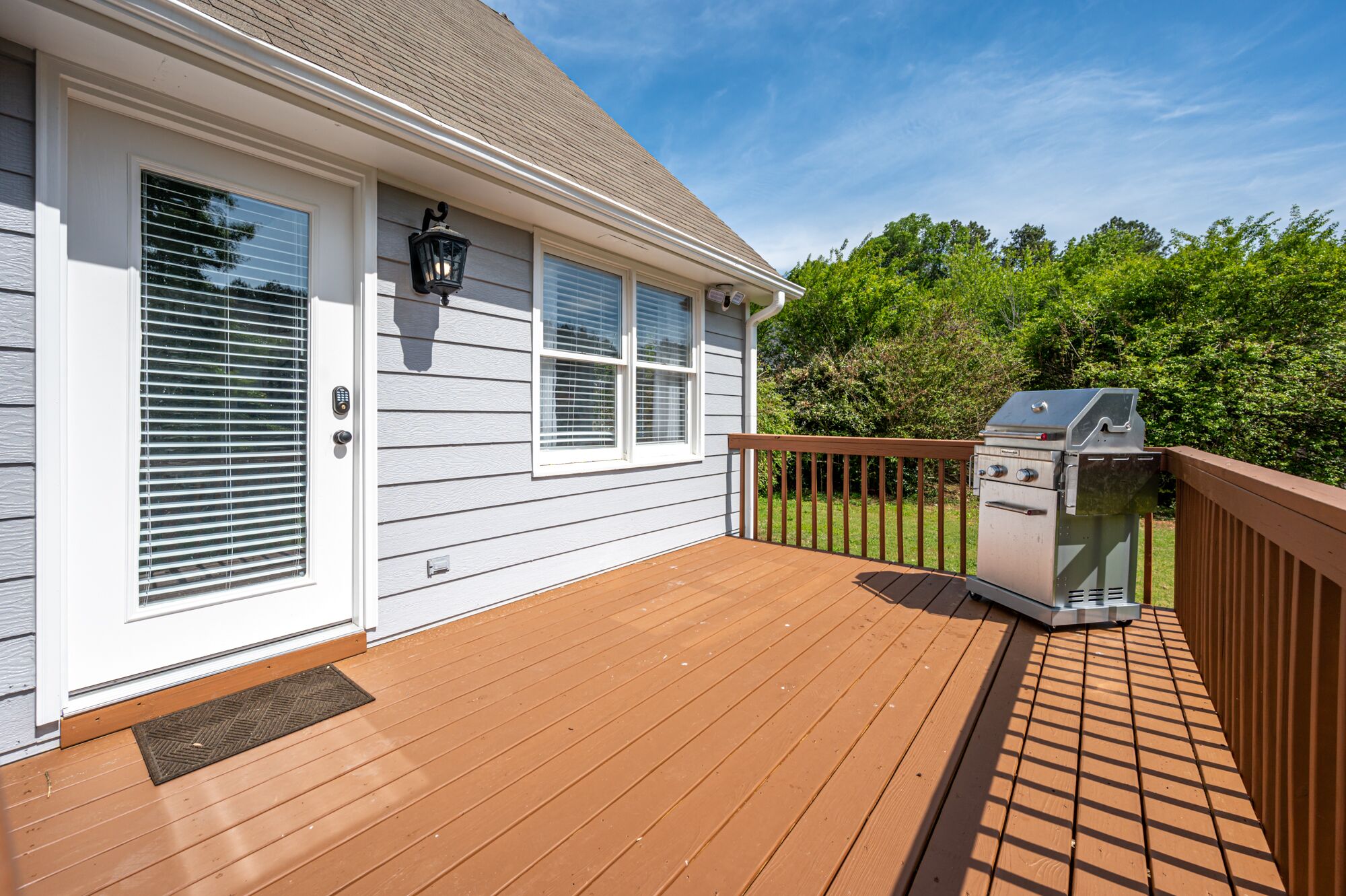 A deck with a barbecue grill, a house with white siding, and a wooden railing.