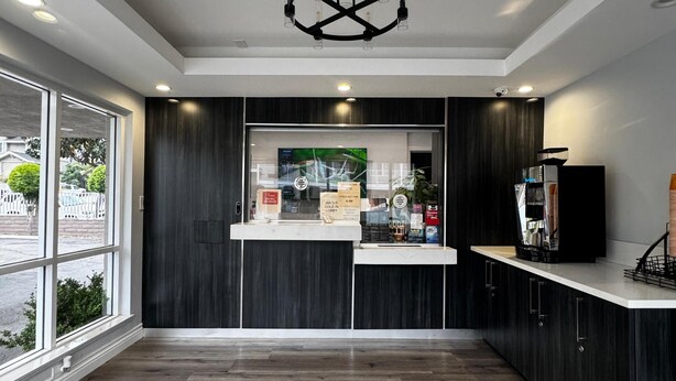 A modern reception area with a counter, dark wood paneling, a large window, and a unique ceiling light fixture. - Friendship Motor Inn (Los Angeles)