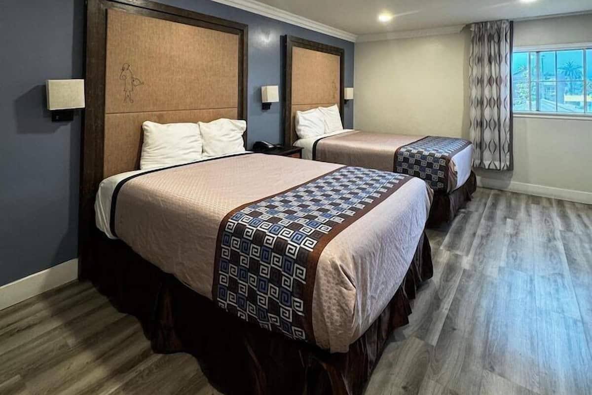A hotel room with two beds, wooden flooring, and a window with curtains.