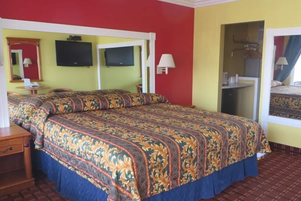 A hotel room with a large bed, a desk, a chair, a mirror, and a television.