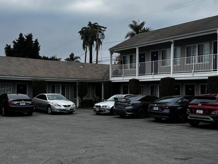 A parking lot with several cars parked in front of a motel with a balcony on the second floor.