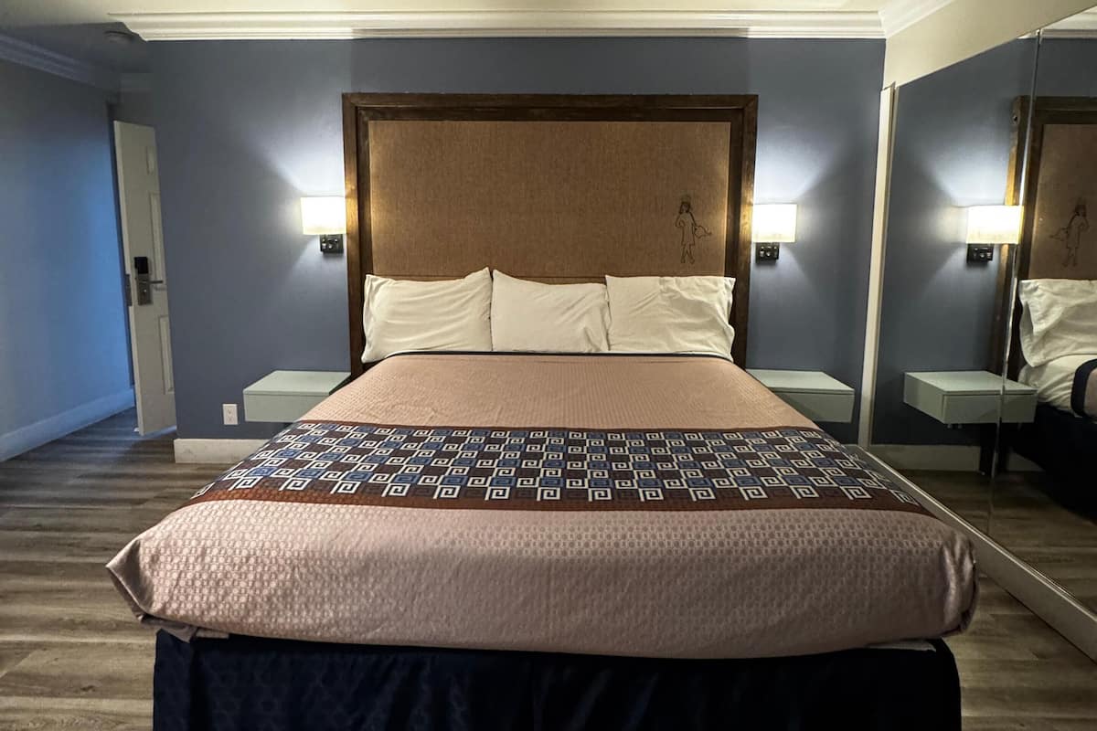 A hotel room with a large bed, a headboard with a light fixture, bedside tables, and a mirror.