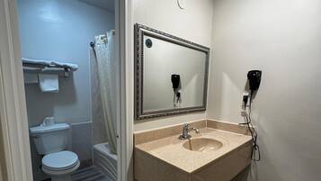 Une salle de bain avec un plancher en bois, un lavabo avec un miroir, des toilettes et un rideau de douche.