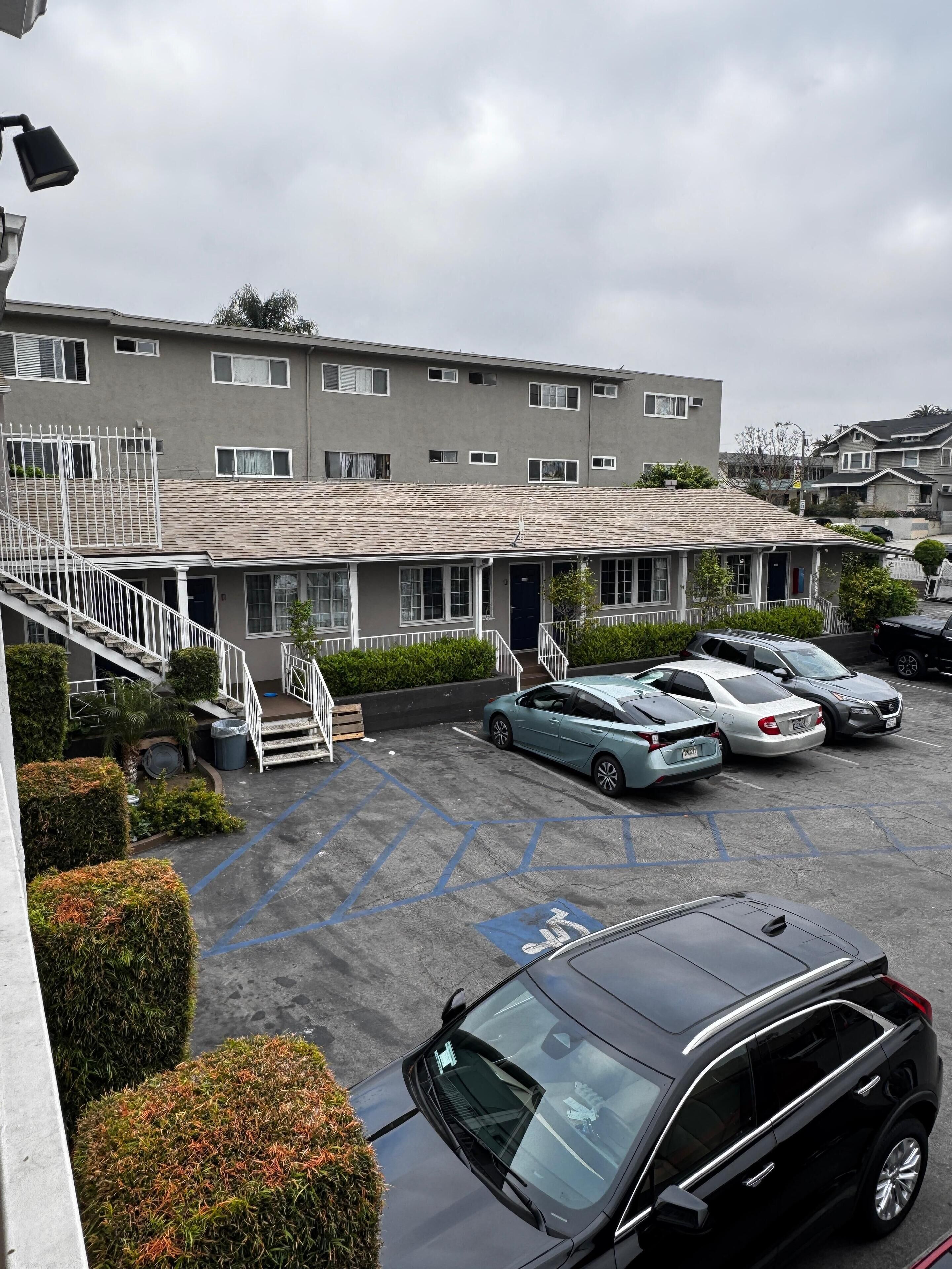 A parking lot with several cars, a building with a flat roof, and a staircase leading to a balcony.