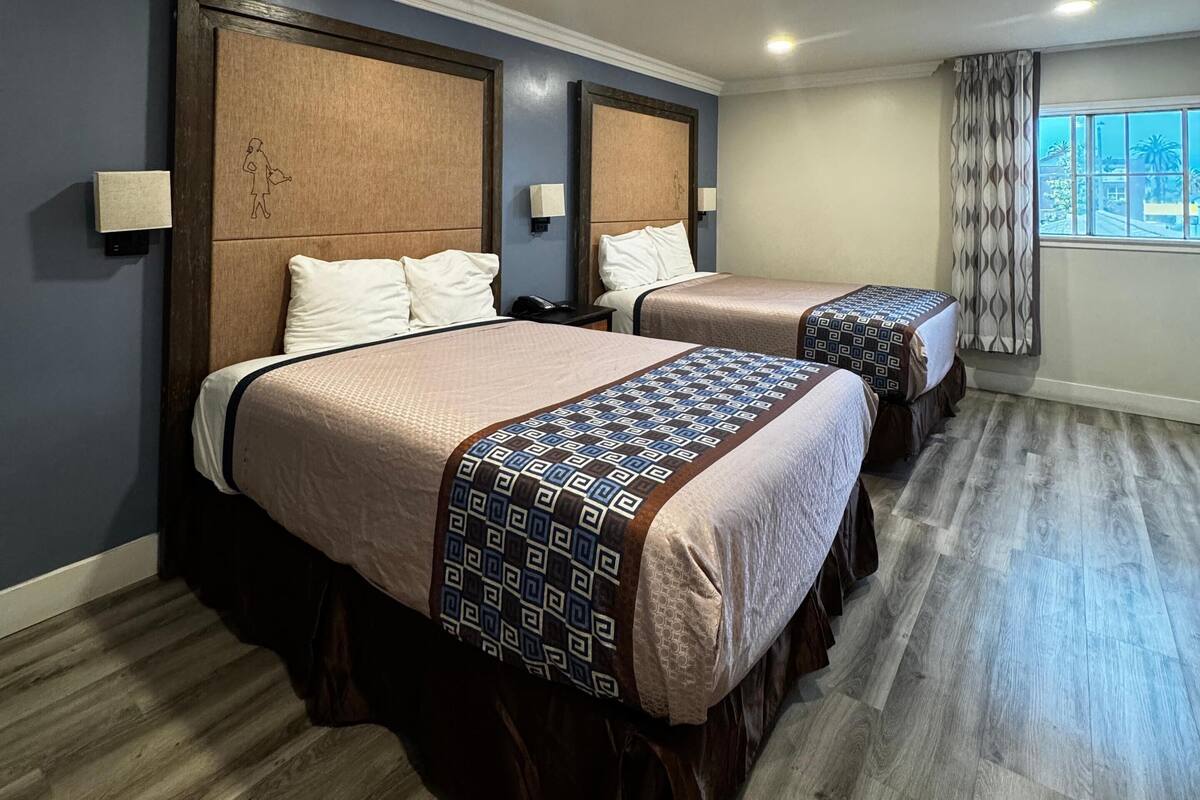 A hotel room with two beds, a large window with curtains, and a wooden floor.