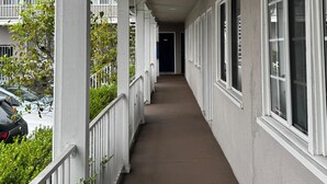 A covered corridor with white railings, large windows, and a concrete floor. - Friendship Motor Inn (Los Angeles)