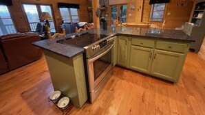 A spacious kitchen with a central island, wooden cabinets, and a stone accent wall. - Spacious Blue Ridge Mountain Cabin. Great location & beautiful views!  (Morganton)