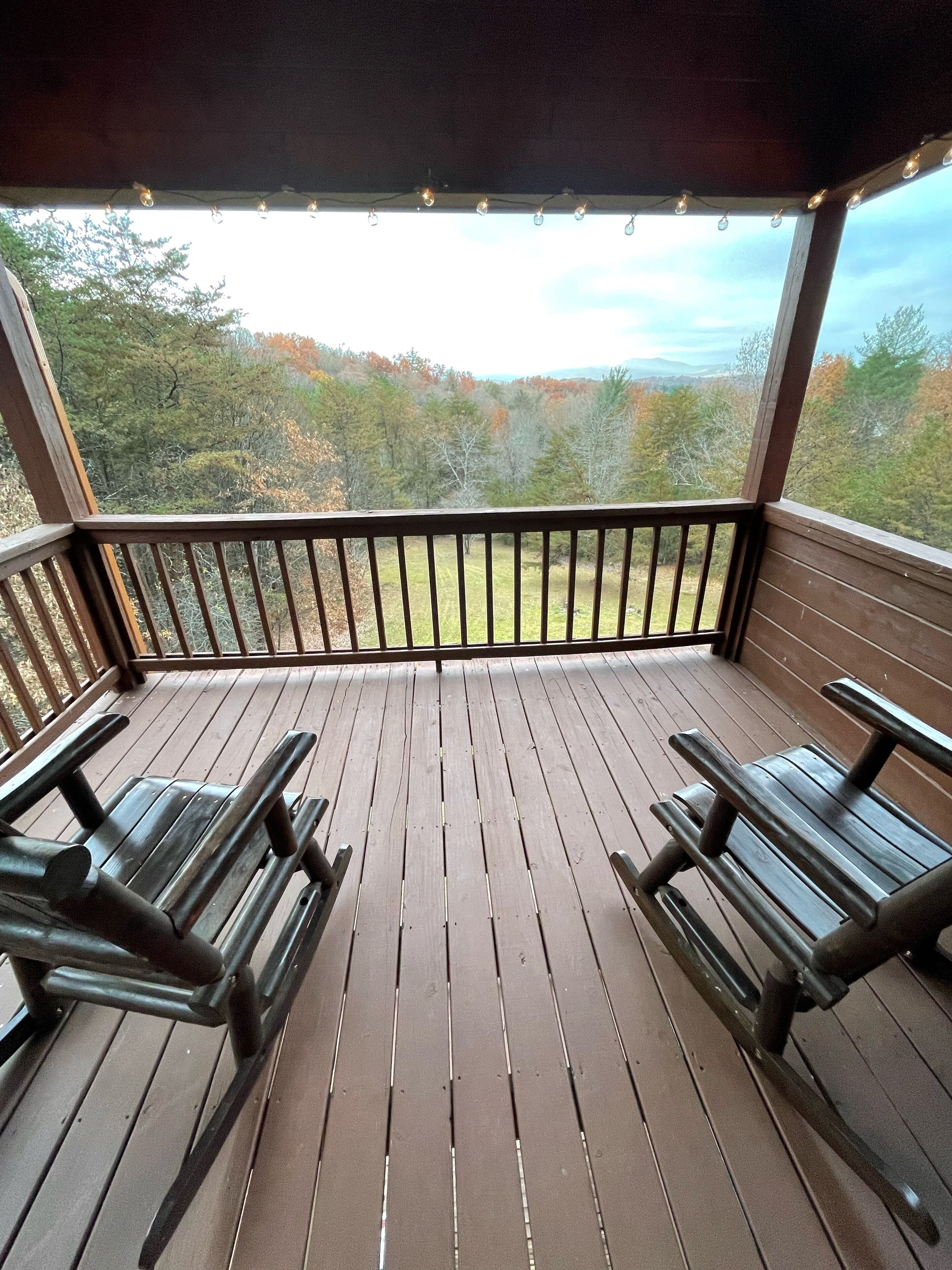 A wooden deck with picnic tables, a railing, and a view of trees and mountains.