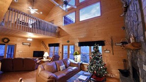 A cozy cabin interior with a wooden interior, a fireplace, a Christmas tree, and a balcony with a railing. - Spacious Blue Ridge Mountain Cabin. Great location & beautiful views!  (Morganton)