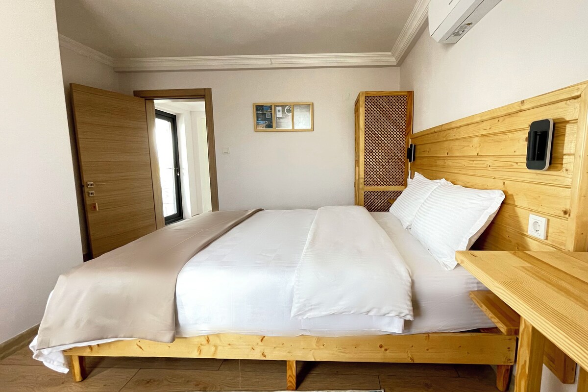 A bedroom with a wooden bed frame, white bedding, a wooden nightstand, and a door leading to another room.
