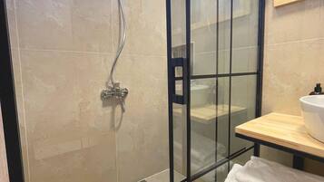 Un baño moderno con ducha envuelta en vidrio, tocador de madera y espejo sobre el lavabo.