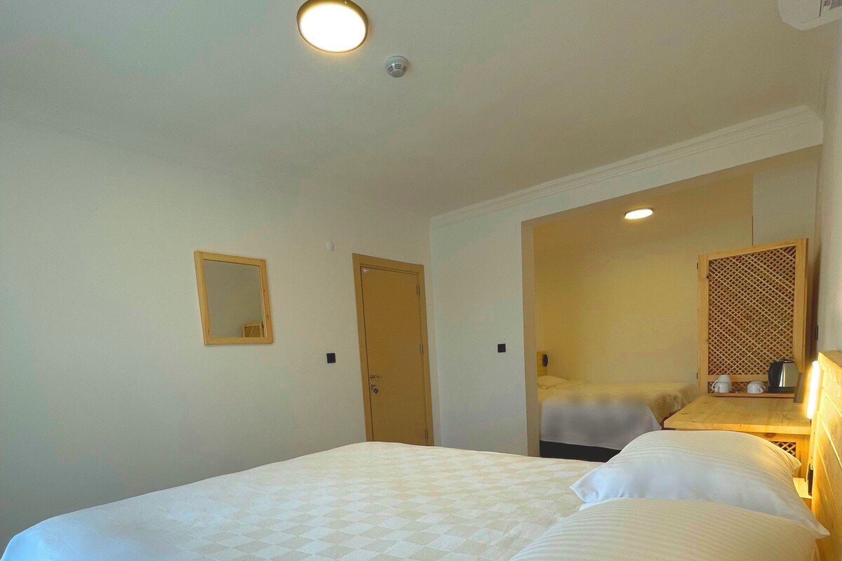 A hotel room with a large bed, a wooden headboard, a small bedside table with a lamp, and a mirror on the wall.