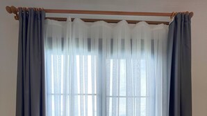Una habitación con un amplio ventanal cubierto por cortinas blancas traslúcidas y cortinas grises oscuras.