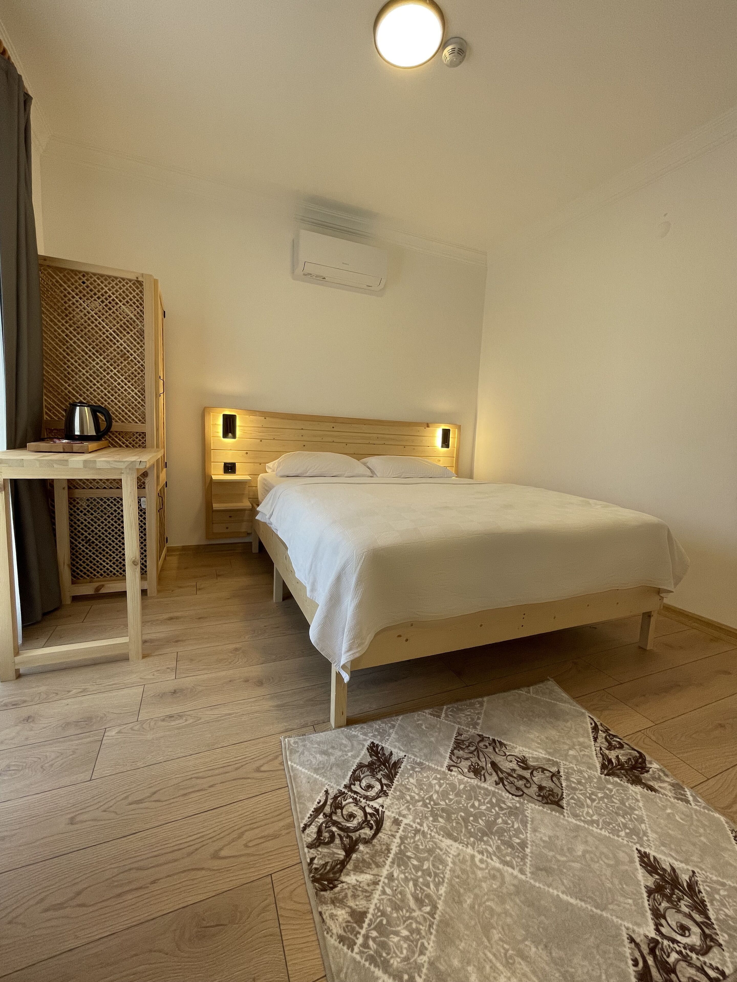 A bedroom with a wooden bed, bedside tables, a small desk, a radiator, and a patterned rug.