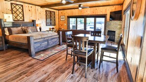 A wooden cabin interior with a bed, dining table, chairs, a fireplace, and a ceiling fan. - Waterfront Lookout (Bolton)