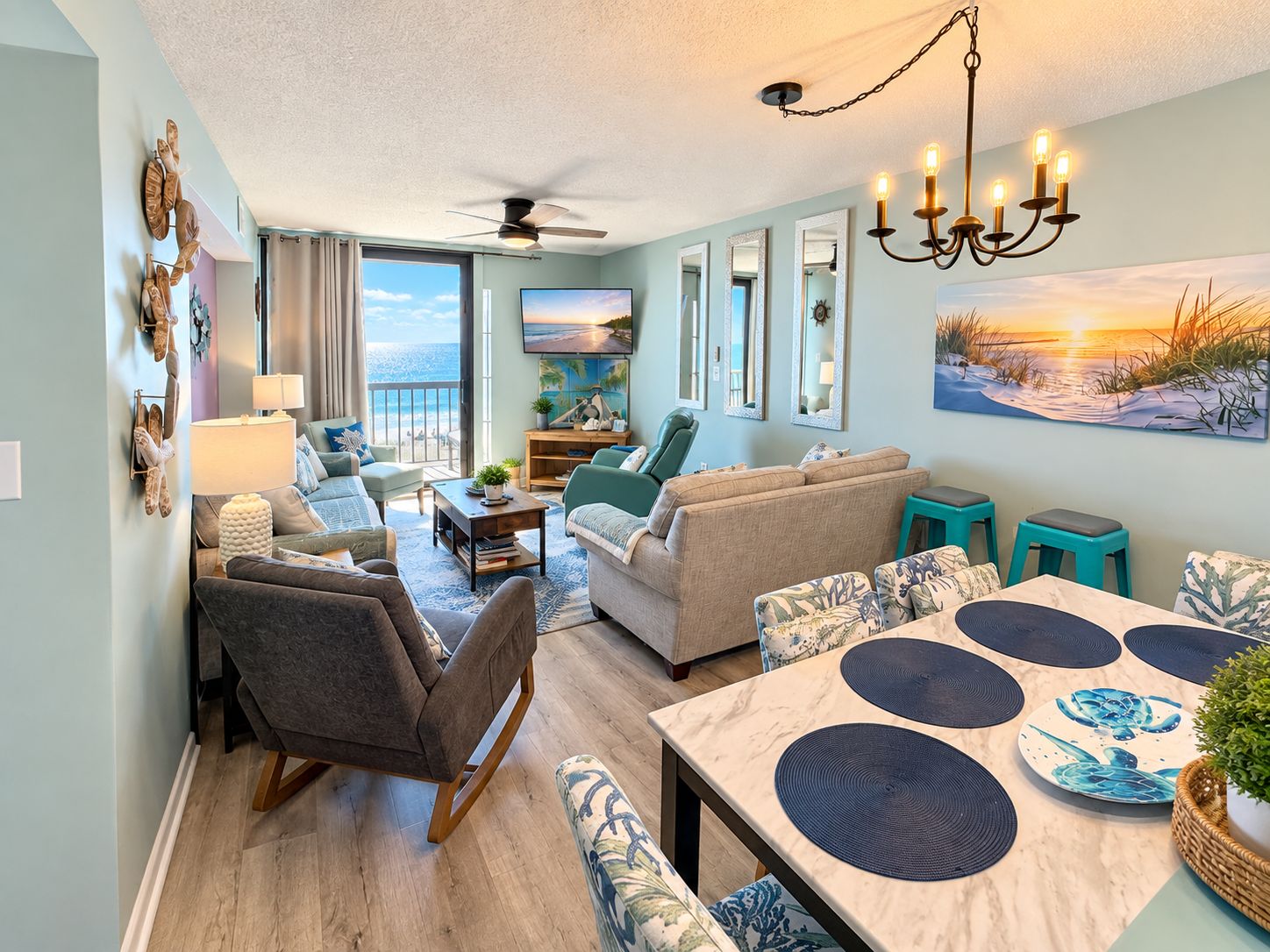 A spacious living area with a view of the ocean, a dining table with placemats, and a ceiling fan.