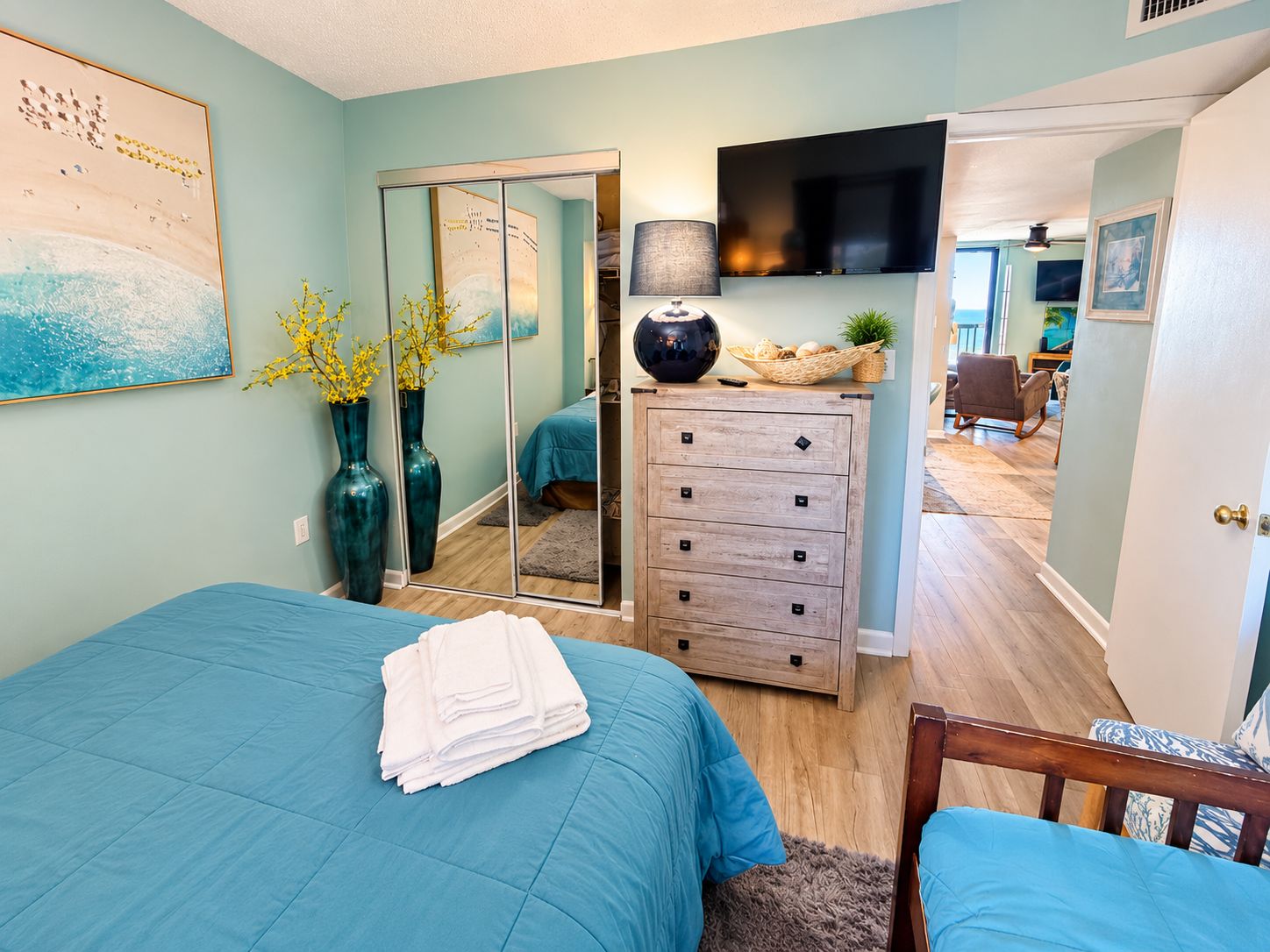 Quarto com cama, cômoda, espelho e televisão.