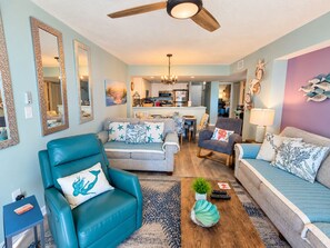 A spacious living room with a teal armchair, a grey sofa, and a wooden coffee table.
