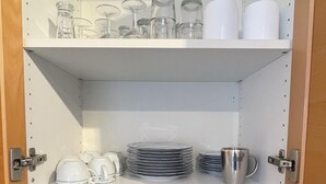 Una cocina con armarios blancos, un tostador, una tetera y varios vasos y platos en las repisas.