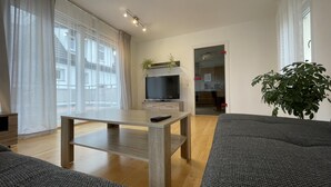 Una sala moderna con una mesa de centro de madera, un sofá gris, un televisor sobre un mueble bajo y una planta.