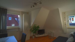 Una habitación pequeña y bien iluminada con una televisión, una planta y una ventana con cortinas.