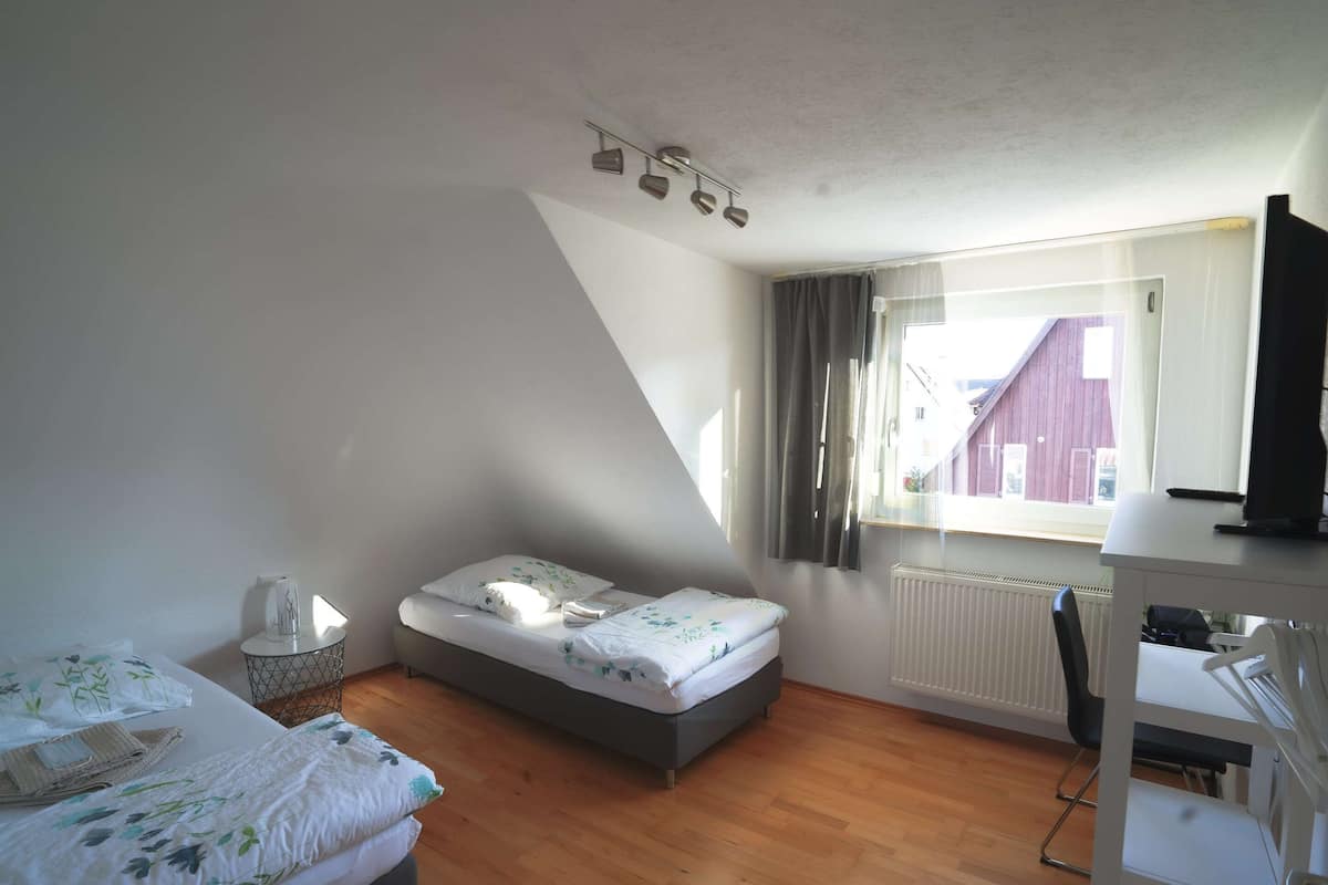 A small, well-lit room with a bed, a desk, and a radiator.