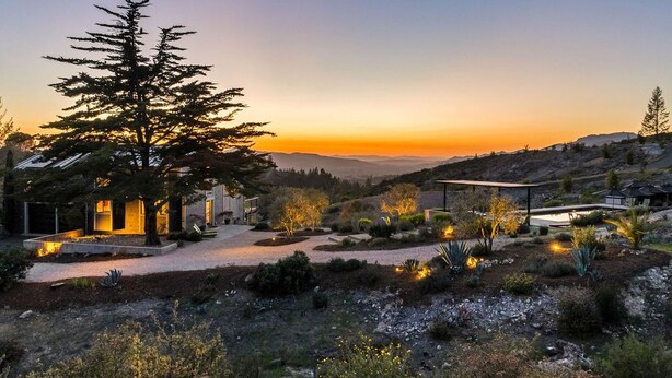 Una casa moderna con un gran árbol en el jardín delantero, un jardín bien cuidado y vistas a las colinas al fondo.