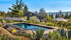 Una casa moderna con piscina, rodeada de exuberante vegetación y un cielo azul despejado.