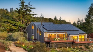 Una casa moderna con techo solar, una terraza con sillas y una escalera de piedra que conduce a la entrada.