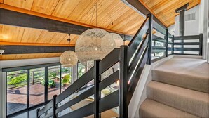 Una escalera de madera con barandillas negras que da a un balcón con vistas a zonas verdes.