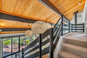 A staircase with a wooden finish and black railings, leading to a balcony with a view of greenery.