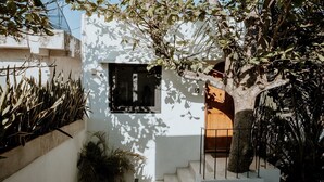 A modern house with a white exterior, a wooden door, and a window. There are plants and a staircase leading to the entrance. - Apartments & Suites MADRE Holbox Self-Check IN (Isla Holbox)
