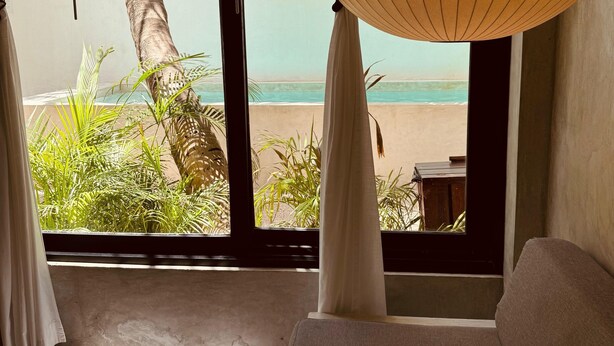 A room with a large window, white curtains, a hanging lamp, and a view of the beach. - Apartments & Suites MADRE Holbox Self-Check IN (Isla Holbox)