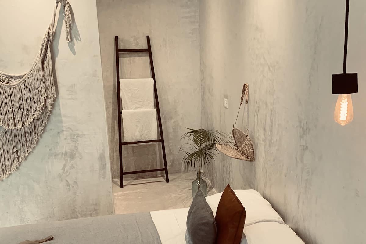 Une chambre à coucher moderne avec un lit, des oreillers, une plante suspendue, une échelle et un luminaire.