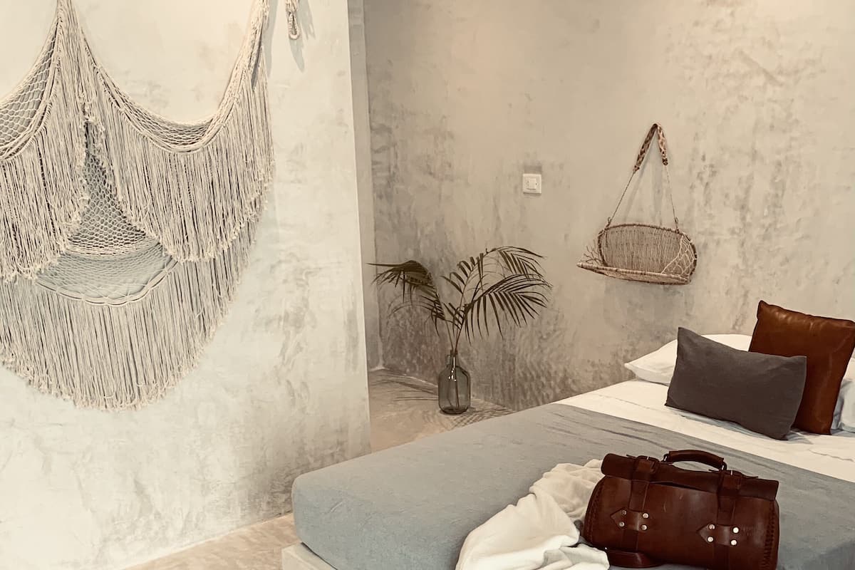 Une chambre à coucher moderne avec un lit, des décorations murales en macramé, un fauteuil suspendu et une plante en pot.
