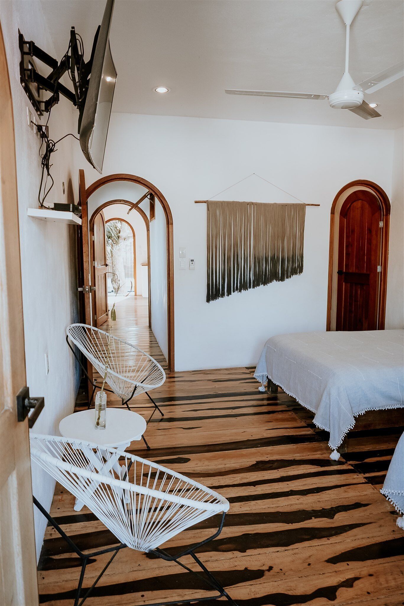 Quarto com cama, televisão na parede, ventilador de teto e piso de madeira.